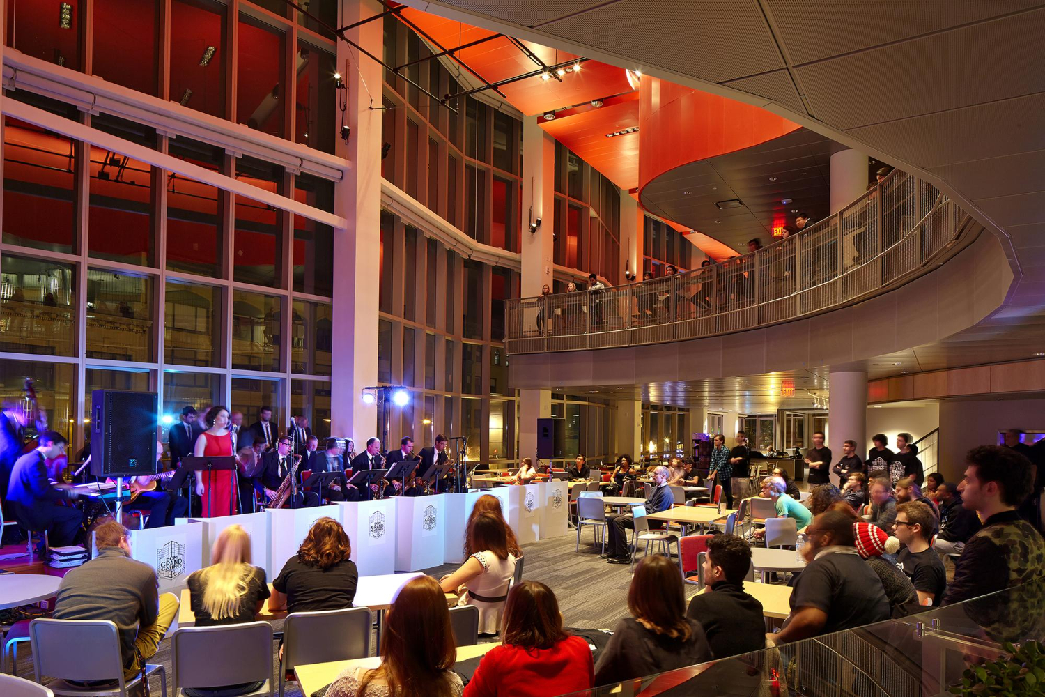 Modern indoor event with live music performance and diverse audience seated at tables in a vibrant, multi-level venue.